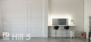 Romantic photo studio with white frames wall, gold bellman cart and white concrete for rental in Los Angeles