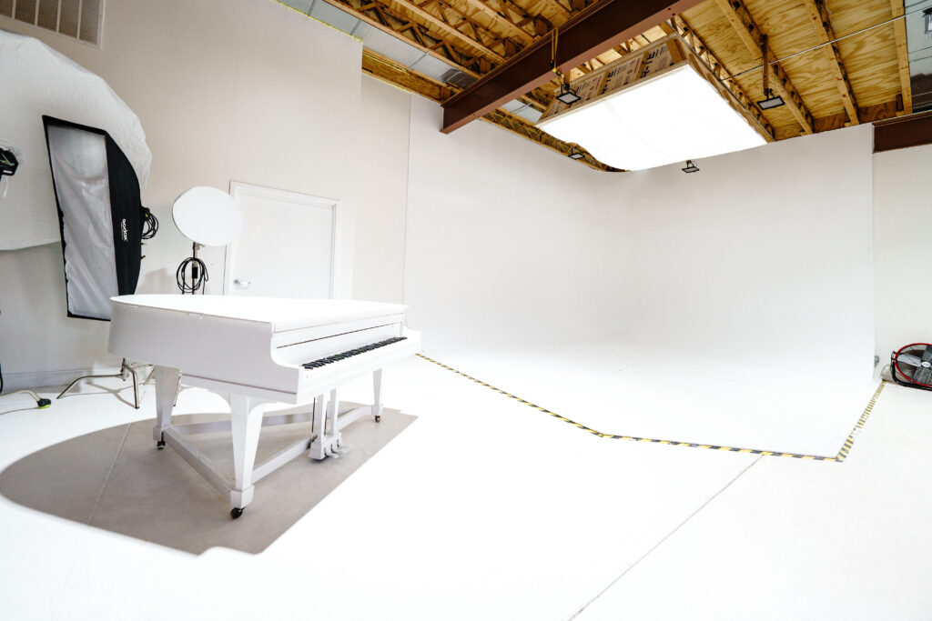 Large daylight photo studio with cyc-wall, tall windows, grand piano, and wooden platform near you Chicago 2
