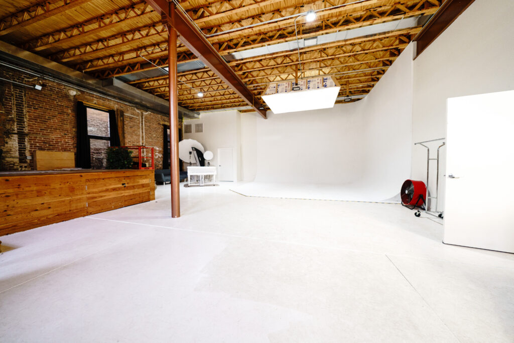 Large daylight photo studio with cyc-wall, tall windows, grand piano, and wooden platform near you Chicago 2